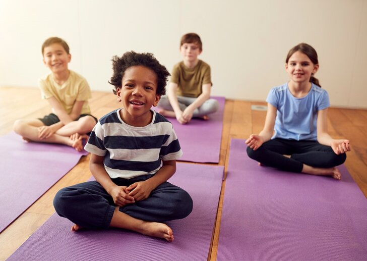 Schulkinder sitzen auf dem Boden auf Übungsmatten | © iStock/monkeybusinessimages